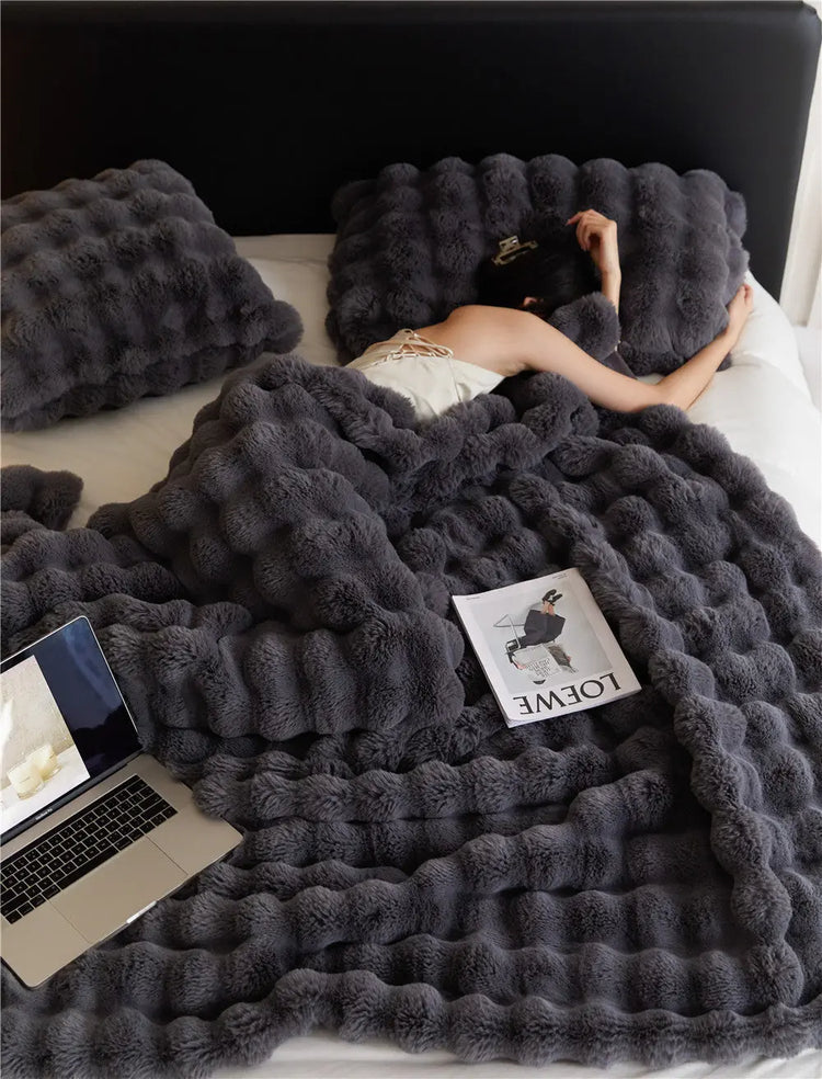 Mörkgrå mjuk och tjock filt för vinter på en säng med person som vilar och laptop intill