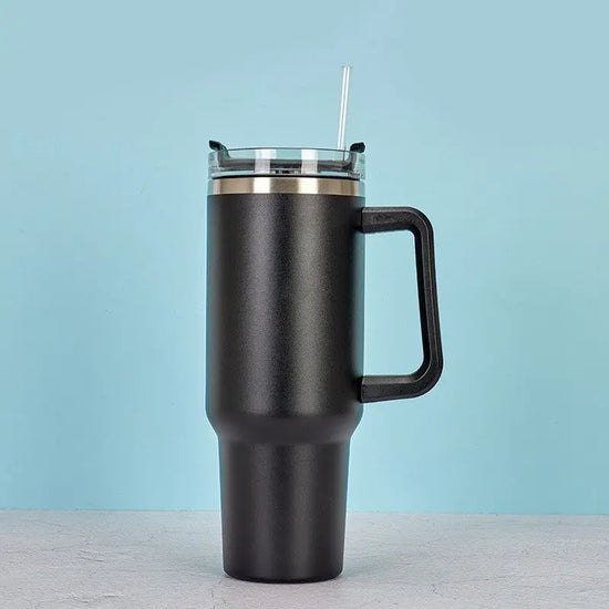 Svart rostfritt stål kaffemugg med handtag och klart lock med sugrör mot ljusblå bakgrund