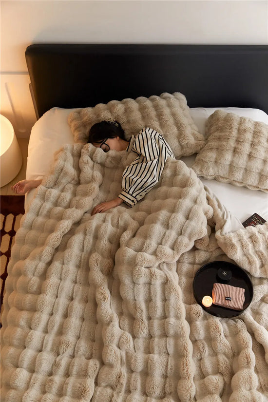 Mjuk och varm tjock filt för vinter i beige färg på en säng med matchande kuddar
