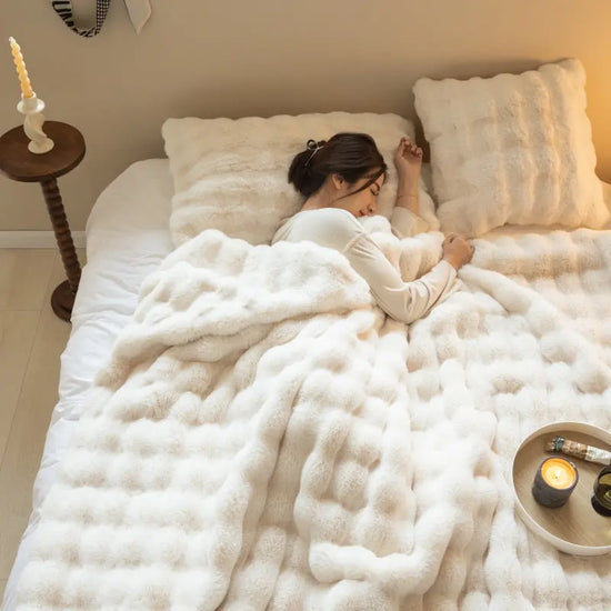 Kvinna som sover under en tjock filt för vinter i vitt med matchande kuddar i mysigt sovrum